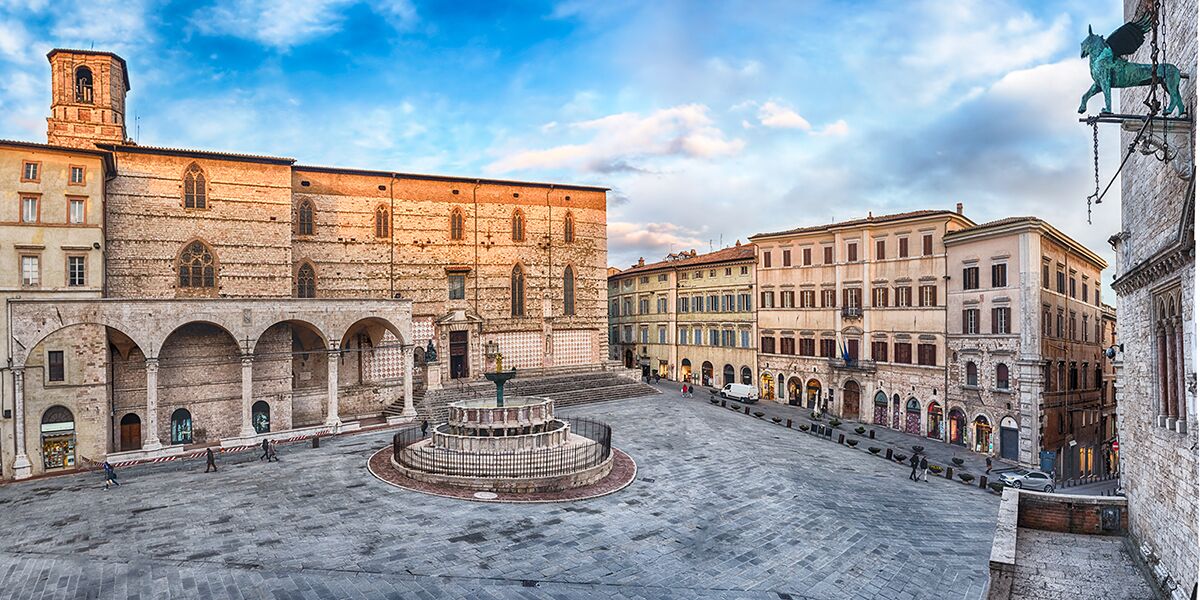 Une vaste cour intérieure agrémentée d’une fontaine centrale, entourée de bâtiments historiques dotés d’arcades et d’une tour imposante.