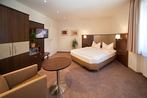 A hotel room with a bed, a TV, a desk, a chair, and a plant. - Hotel Engel (Rheinmunster)