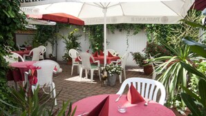 An outdoor patio with white chairs and tables, covered by a white umbrella. - Hotel Engel (Rheinmunster)
