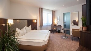 A hotel room with a large bed, a desk, a chair, a small table, a potted plant, and a mirror. - Hotel Engel (Rheinmunster)