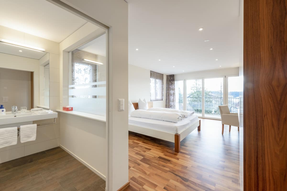 A modern bedroom with a large bed, a bathroom with a mirror, and a view of the outdoors.