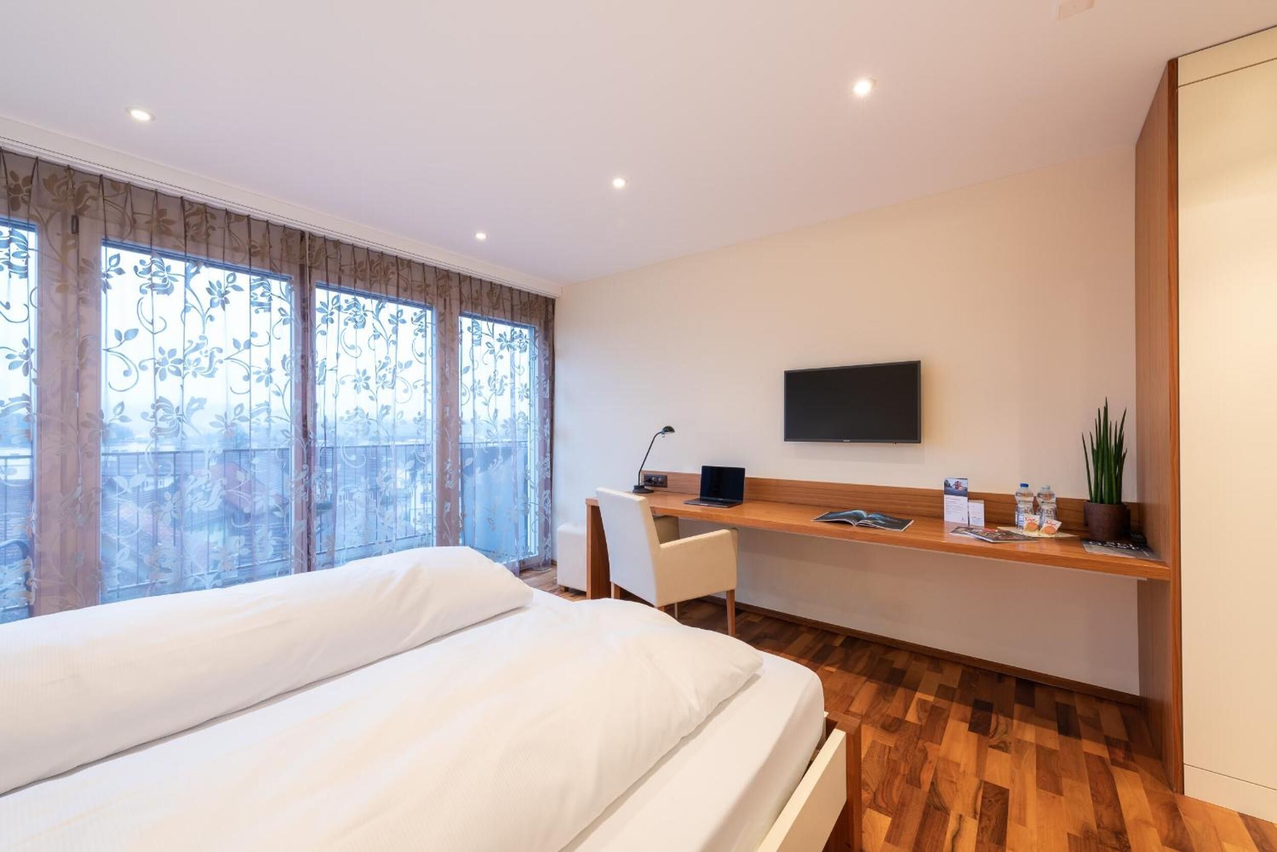 Une chambre d’hôtel moderne dotée d’un grand lit, d’un bureau avec un ordinateur, d’une télévision à écran plat et d’une fenêtre avec des rideaux.