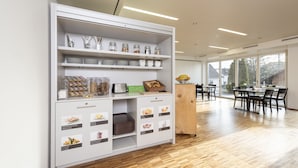 A modern kitchen with white cabinetry, wooden flooring, and a dining area with a table and chairs. - Hotel Rössli (Zuzwil)
