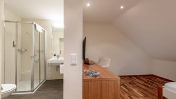 A modern bathroom with a glass shower enclosure, a white sink, and a wooden vanity with a laptop and magazine.