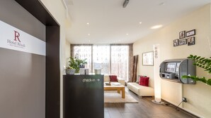 A hotel reception area with a check-in counter, a sofa, and a wall-mounted self-service kiosk. - Hotel Rössli (Zuzwil)