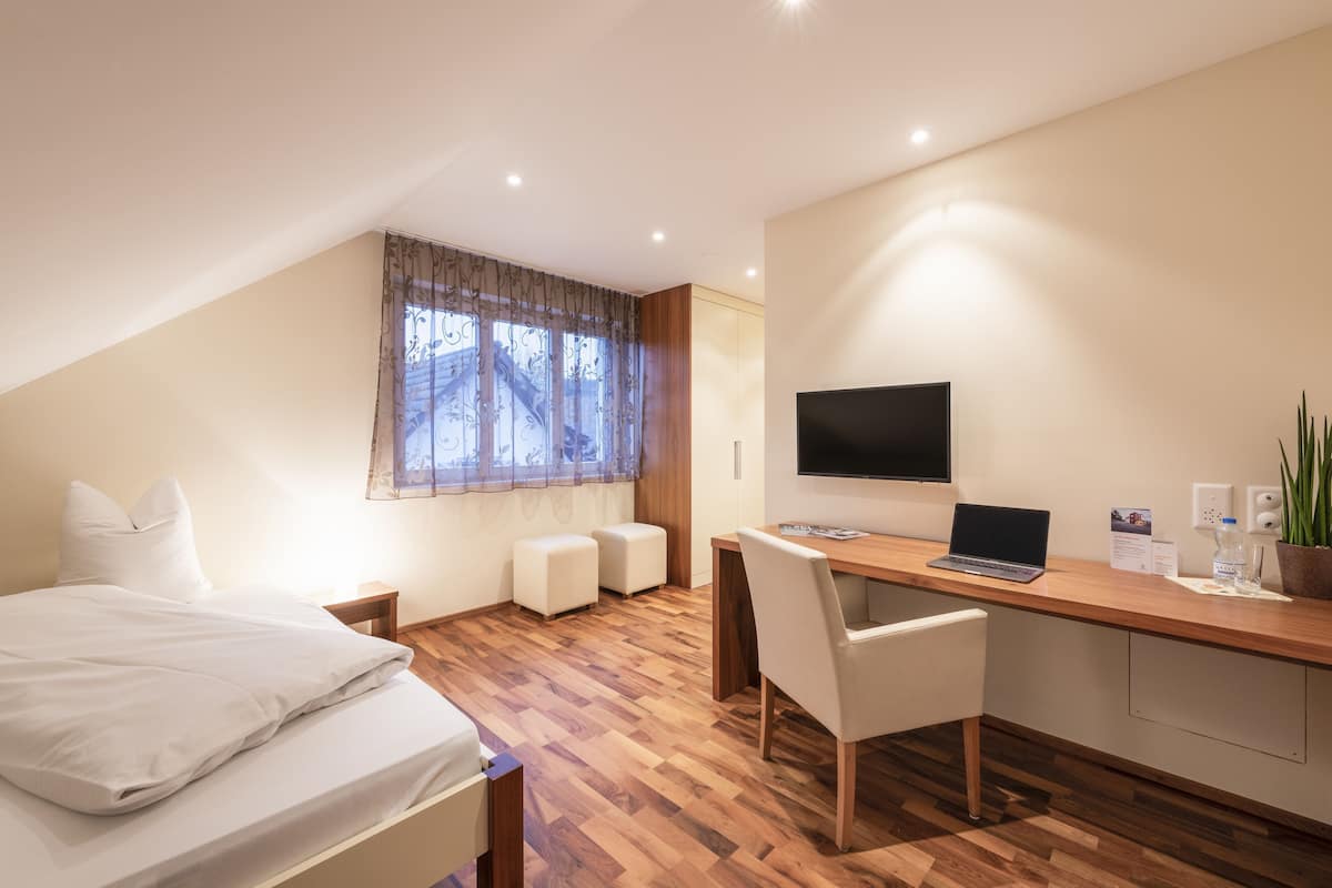 A modern room with a bed, a desk, a chair, a TV, and a window with curtains.