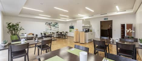 Un comedor moderno con mesas y sillas de madera, manteles individuales verdes y una isla central con pileta y mostrador.