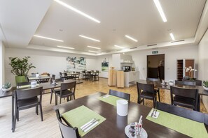 A modern dining area with wooden tables and chairs, green placemats, and a central island with a sink and counter. - Hotel Rössli (Zuzwil)