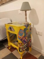 Una mesita de noche amarilla con una lámpara, decorada con varios adhesivos coloridos y un frente de vidrio.