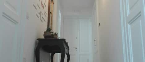 Un couloir avec un tapis à motifs, un luminaire fixé au mur et une porte au fond.