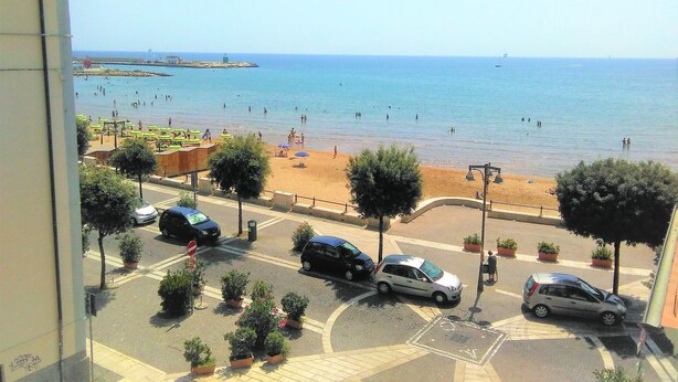 A beach view from a balcony with a clear sky, a sandy beach, and several parked cars. - Déjà Vu (Crotone)
