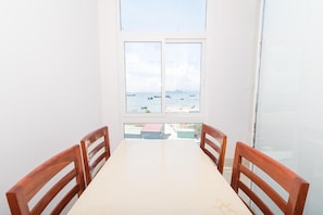 Zona pranzo con tavolo e quattro sedie di legno, ampia finestra vista mare e barche.