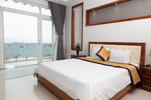 A hotel room with a large bed, a nightstand, a mirror, and a view of the sea through large windows. - Sao Mai Hotel & Apartment (Ho Chi Minh City)