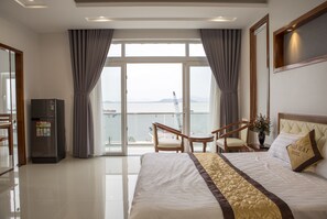 Habitación de hotel con una cama grande, un escritorio, una silla, un refrigerador y vistas al mar.