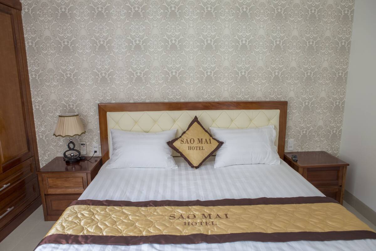 A hotel room with a bed, wooden nightstands, a lamp, and a wall with a floral pattern.