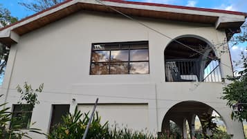 A two-story building with a red roof, a balcony with metal railings, and a window with a view of the sky.