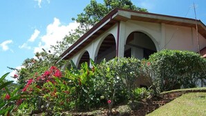 A house with a covered porch, surrounded by lush greenery and flowering plants.