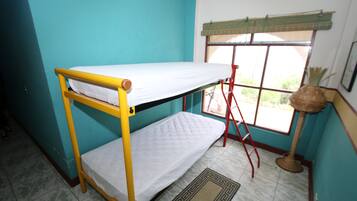 A bunk bed in a room with teal walls, a window with a bamboo blind, and a floor mat.
