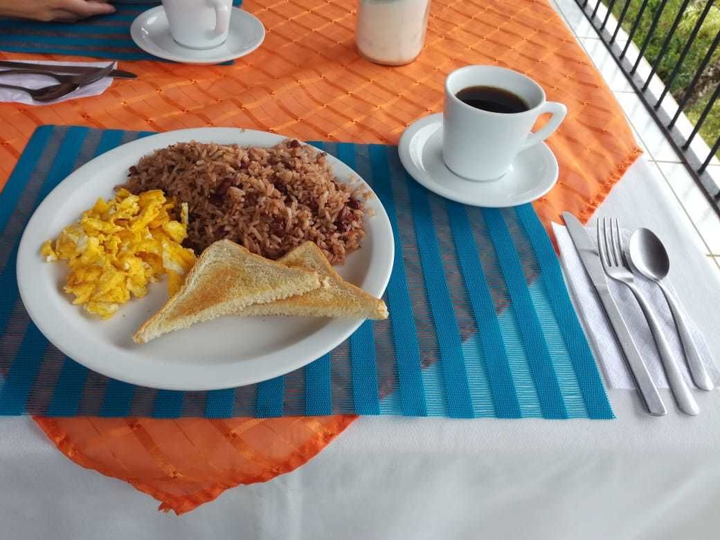 Un plato de desayuno con huevos revueltos, arroz frito y tostadas sobre una mesa con mantel a rayas.