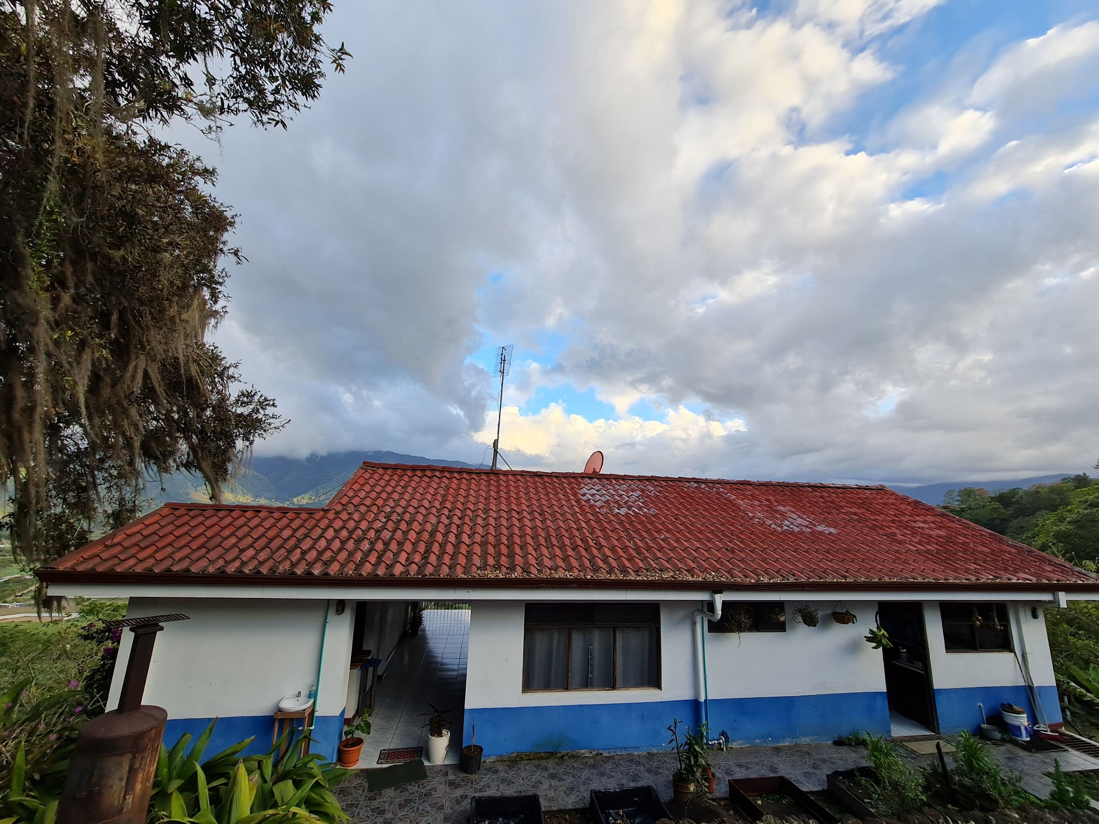 A two-story building with a red-tiled roof, a blue and white exterior, and a view of mountains in the background.