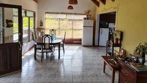 A kitchen with a dining area, a refrigerator, and a window with a view of greenery.