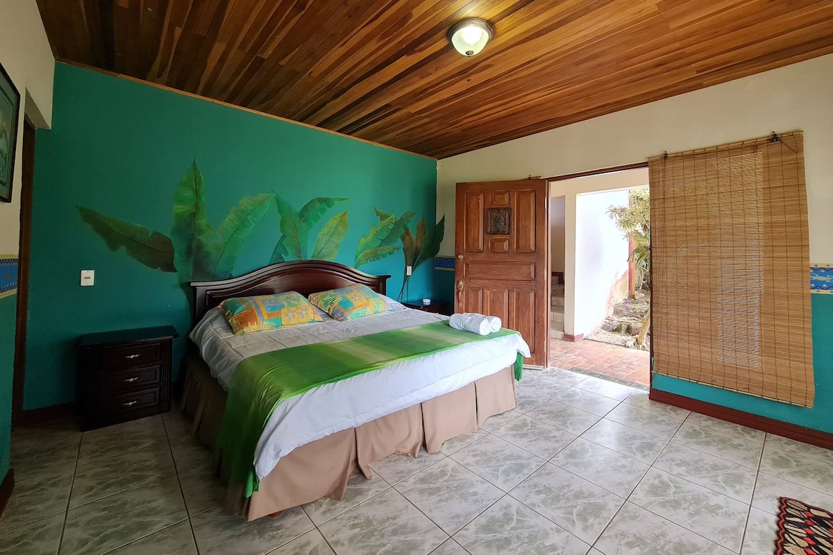 A bedroom with a wooden ceiling, a bed with a green and white bedspread, a nightstand, and a door leading to a balcony.
