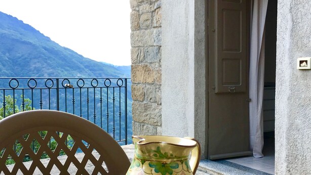 Une table avec quatre tasses en céramique et un pichet, placée sur un balcon donnant sur un paysage montagneux.
