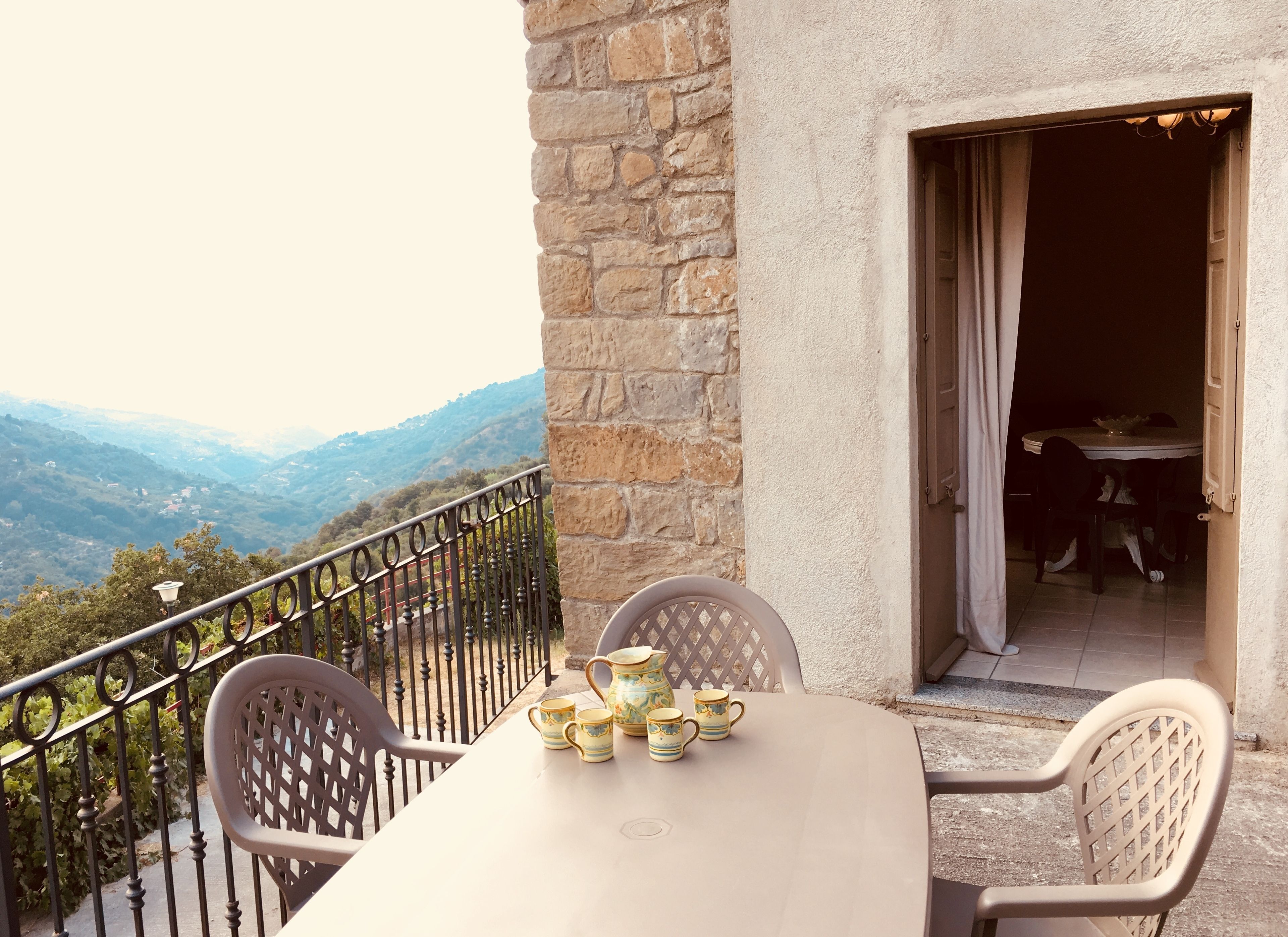 A balcony with a table set for tea, overlooking a mountainous landscape.