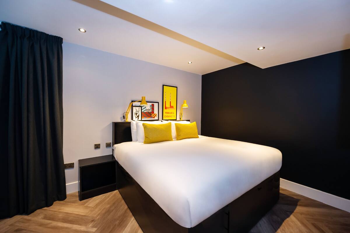 Een moderne hotelkamer met een groot bed, nachtkastje, lamp en een ingelijst schilderij aan de muur.
