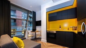 Een moderne keuken met zwarte kasten en een geel aanrecht, een eethoek met een tafel en stoelen, en een bank met een geel kussen.