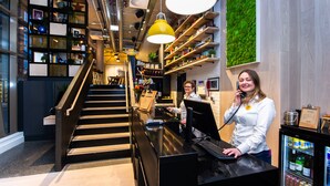 Een moderne hotel lobby met een trap, een receptiebalie en een groene wand.