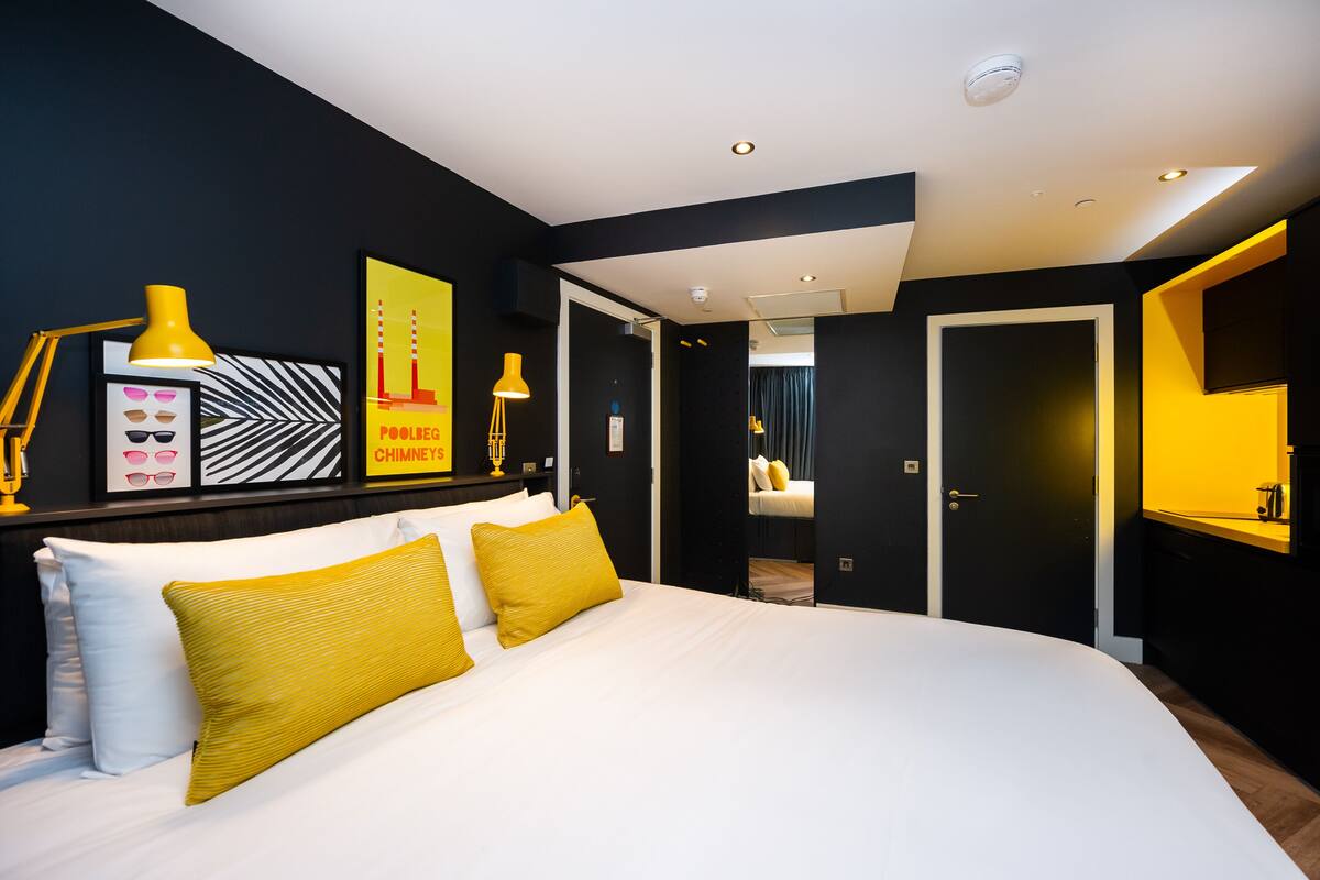 Een moderne hotelkamer met een groot bed, een bureau met stoel, en een zithoek met een stoel en tafel.