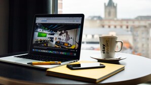 Een laptop op een tafel, met een beker en een notitieboekje ernaast.