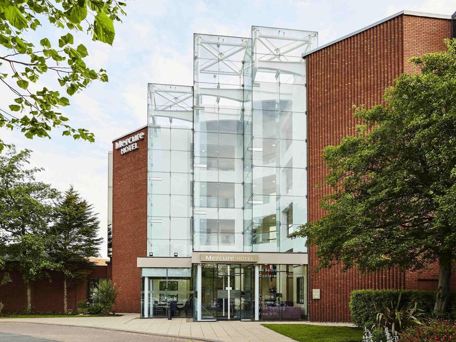 A modern hotel with a glass facade, a brick exterior, and a sign indicating 44 bedrooms and a conference facility.