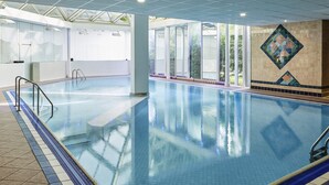 An indoor swimming pool with clear glass walls, a tiled floor, and a geometric tile pattern on the wall. - Mercure St Helens (St Helens)