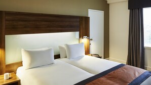 A hotel room with two beds, a nightstand, a lamp, a window with curtains, and a door. - Mercure St Helens (St Helens)