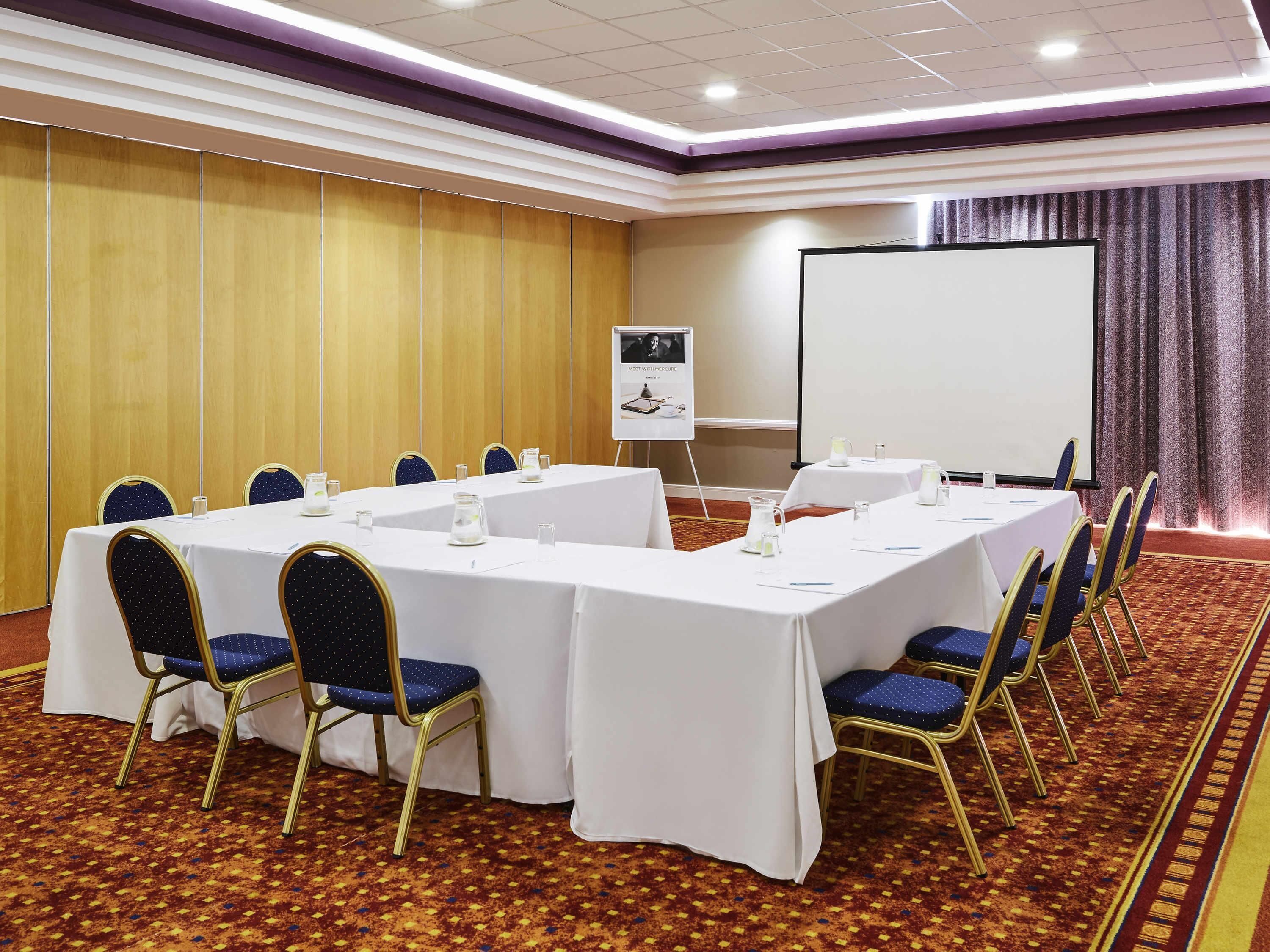 A conference room with a long table, chairs, a projector screen, and a flip chart.