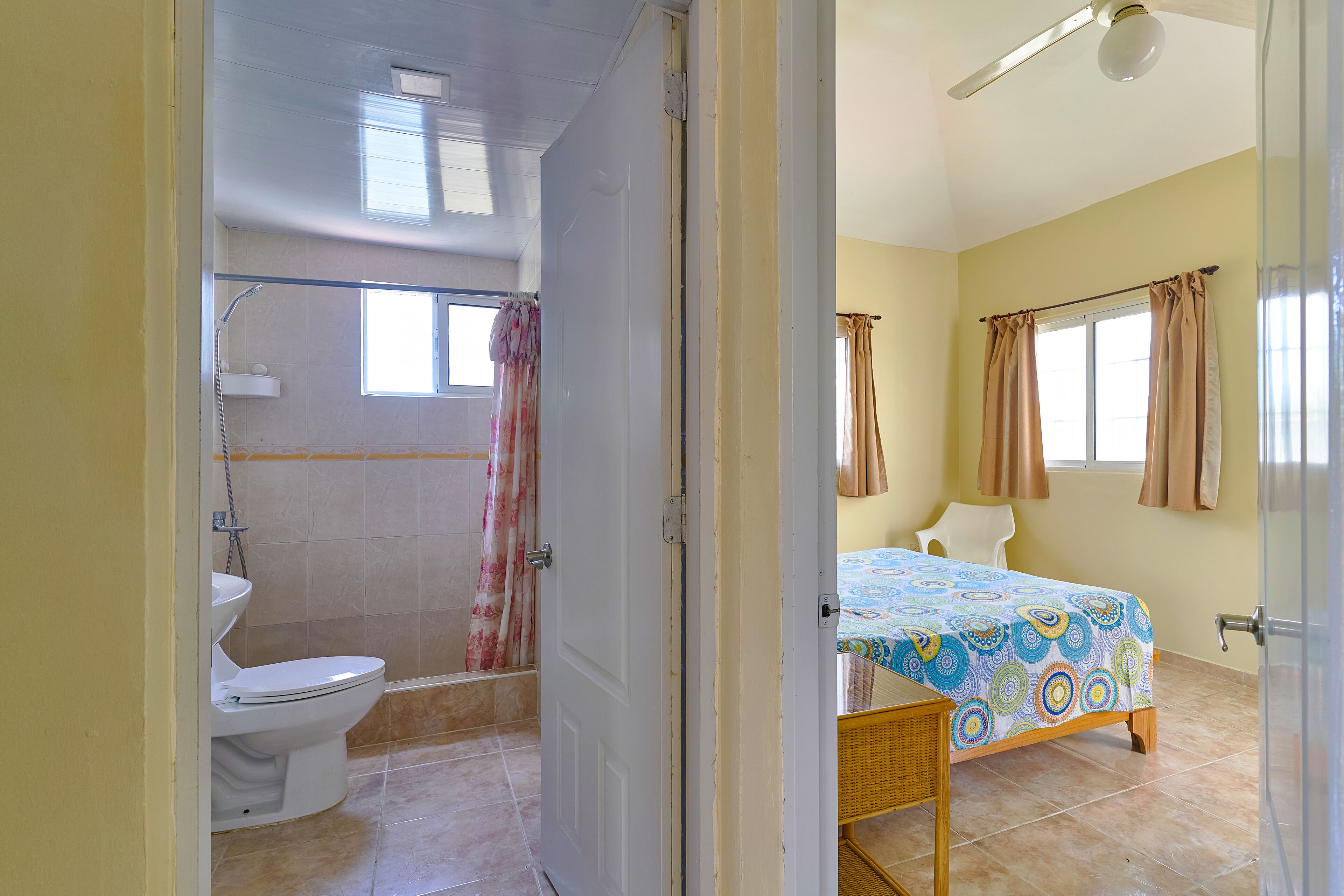 Une salle de bain avec des toilettes, une douche et un lit recouvert d’une courtepointe aux couleurs vives.