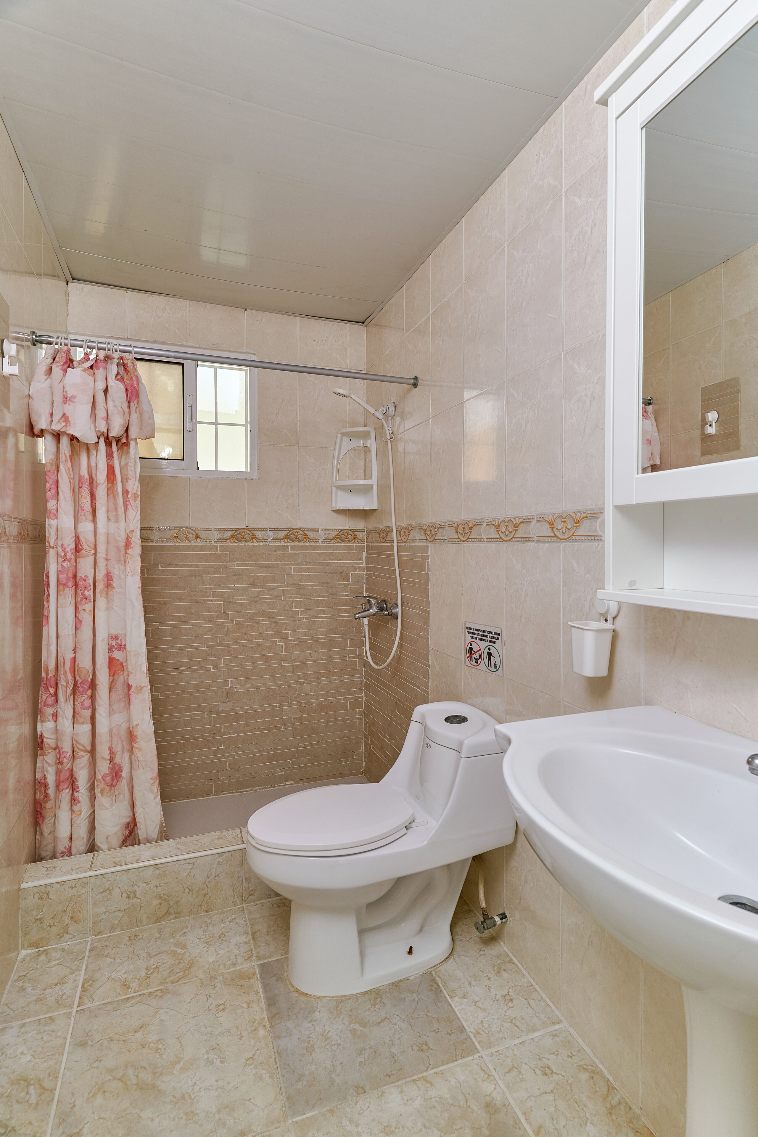 Een badkamer met toilet, wastafel, douche en een raam met gordijn.