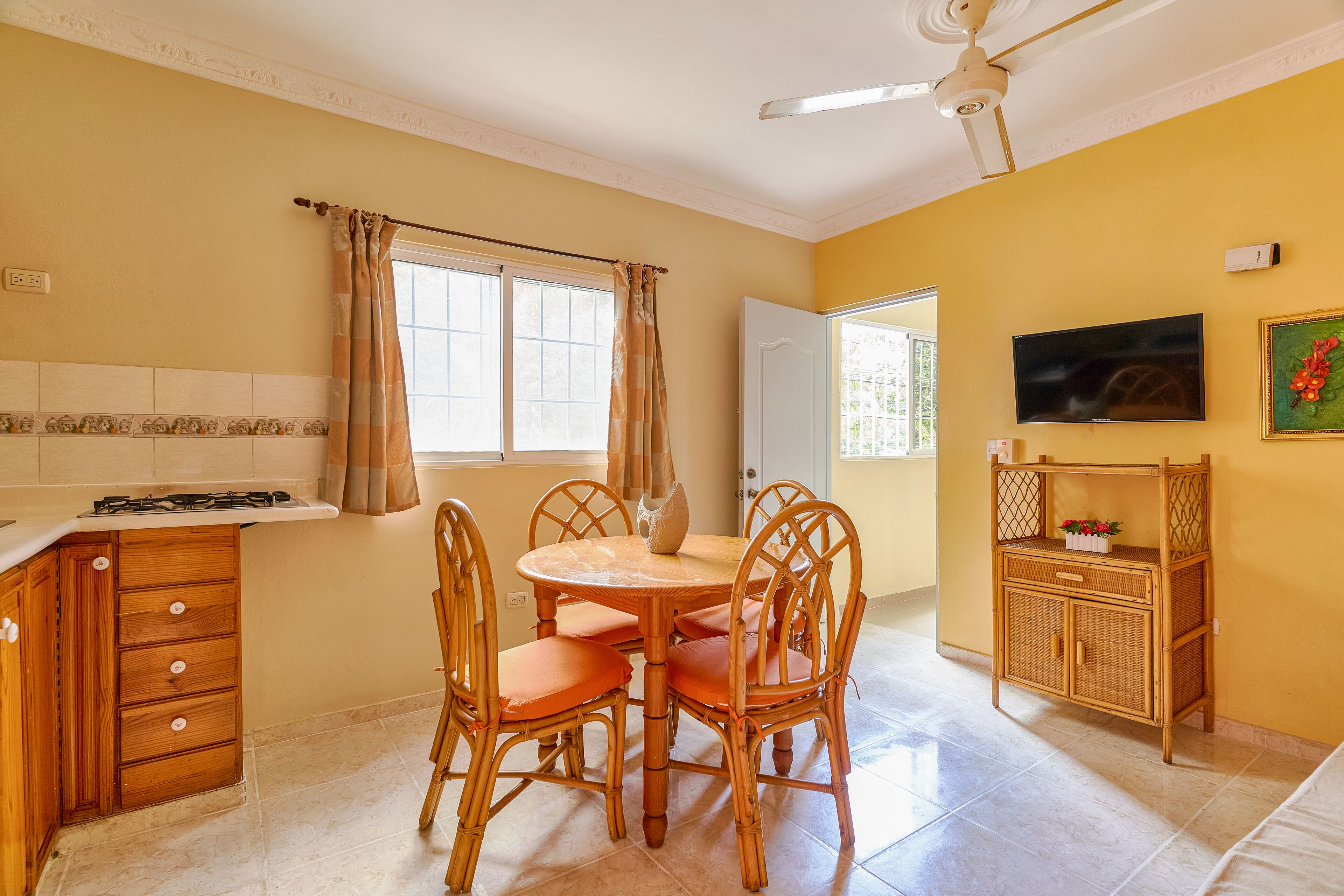 A kitchen with a dining table and chairs, a ceiling fan, and a television on the wall.