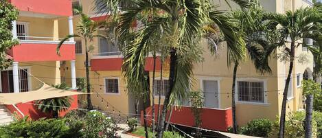 Un edificio a più piani con balconi, una palma e un'area giardino con un vialetto.