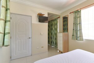 Un dormitorio con cama, armario, televisor montado en la pared y una puerta.