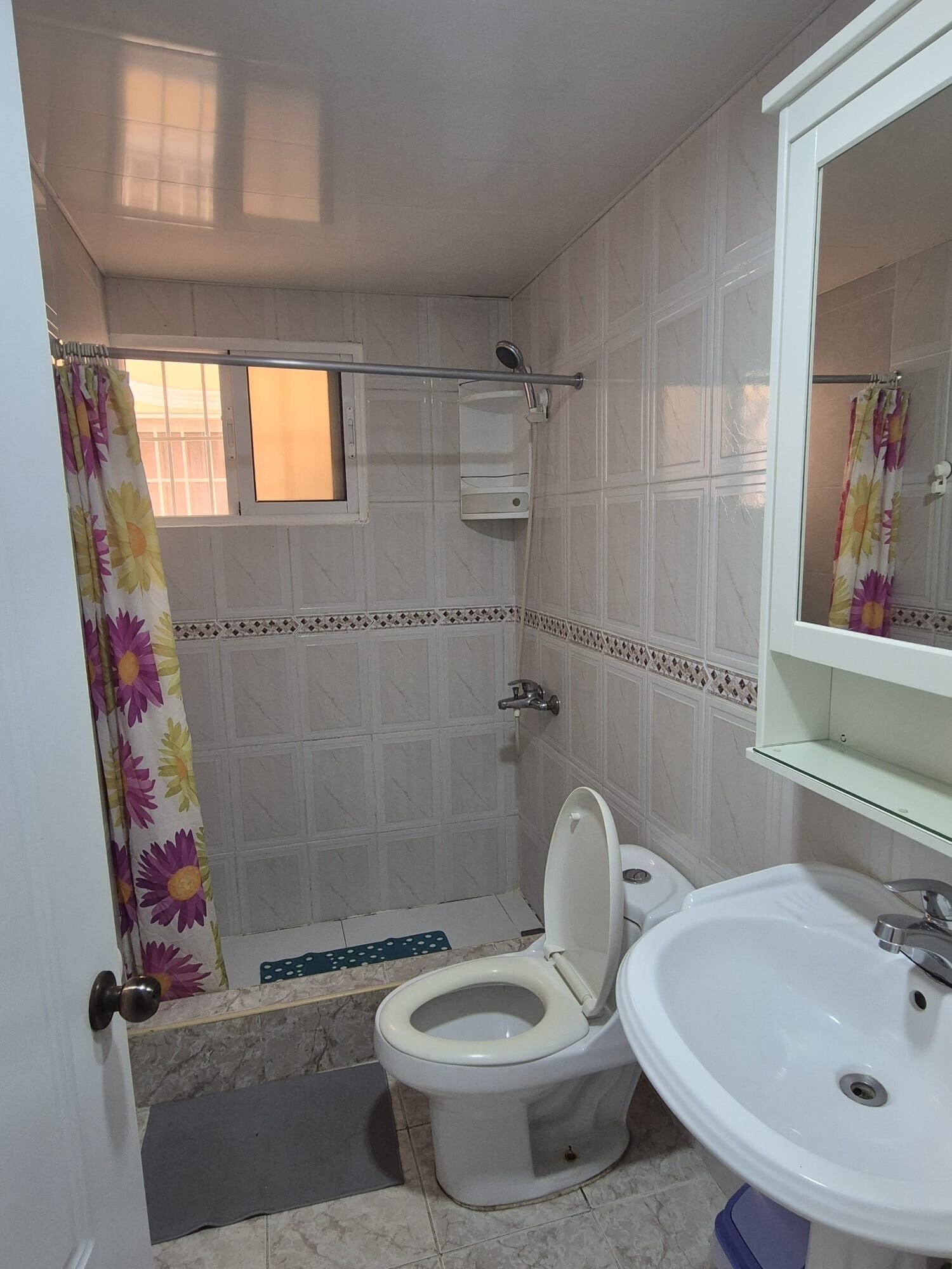 A bathroom with a toilet, sink, shower, and a window with a curtain.