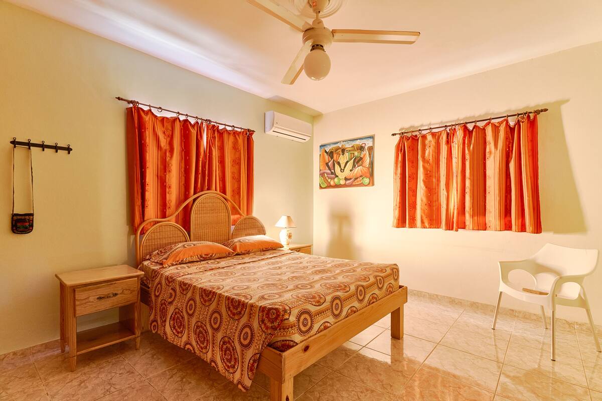 A bedroom with a bed, nightstand, chair, and a ceiling fan.