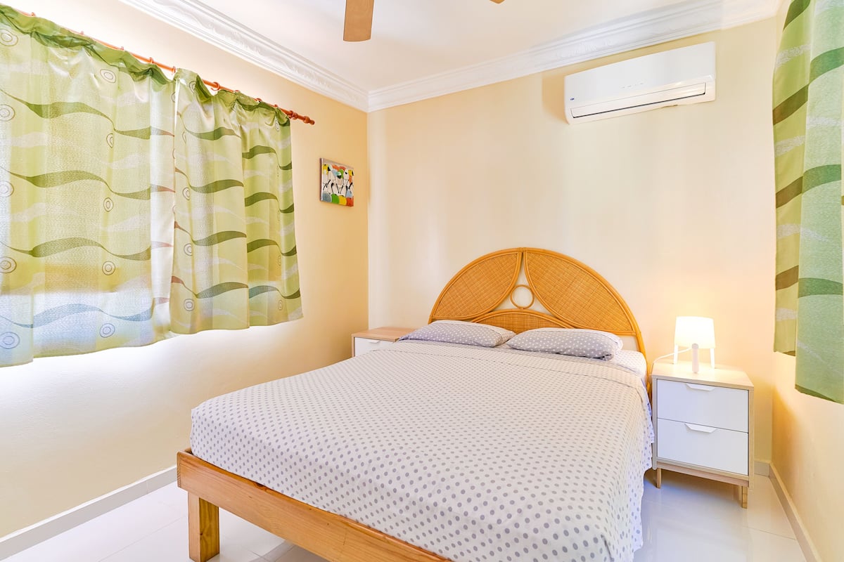 A bedroom with a wooden bed, white nightstand, and a wall-mounted air conditioner.