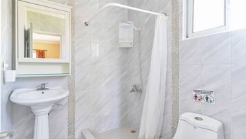 Un baño con lavamanos pedestal, ducha con puerta de cristal y retrete.