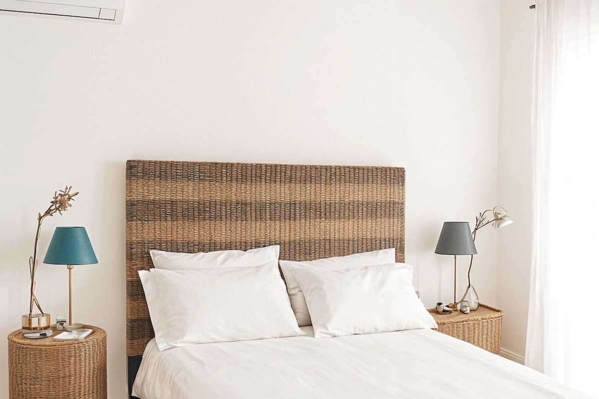 Ein Schlafzimmer mit einem Bett, zwei Nachttischen, einem Deckenventilator, einer gewebten Bank und einer Fußmatte.