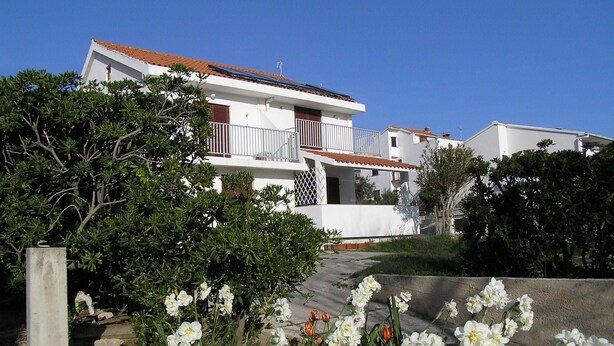 A white two-story house with a red-tiled roof, a balcony, and solar panels on the roof.