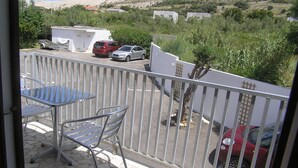A balcony with a table and chairs, overlooking a parking area with several cars and a view of hills and sparse vegetation.
