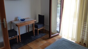 A room with a bed, a table with a chair, a TV mounted on the wall, and a sliding glass door leading to an outdoor area.